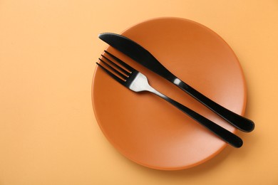 Ceramic plate with cutlery on pale orange background, top view. Space for text