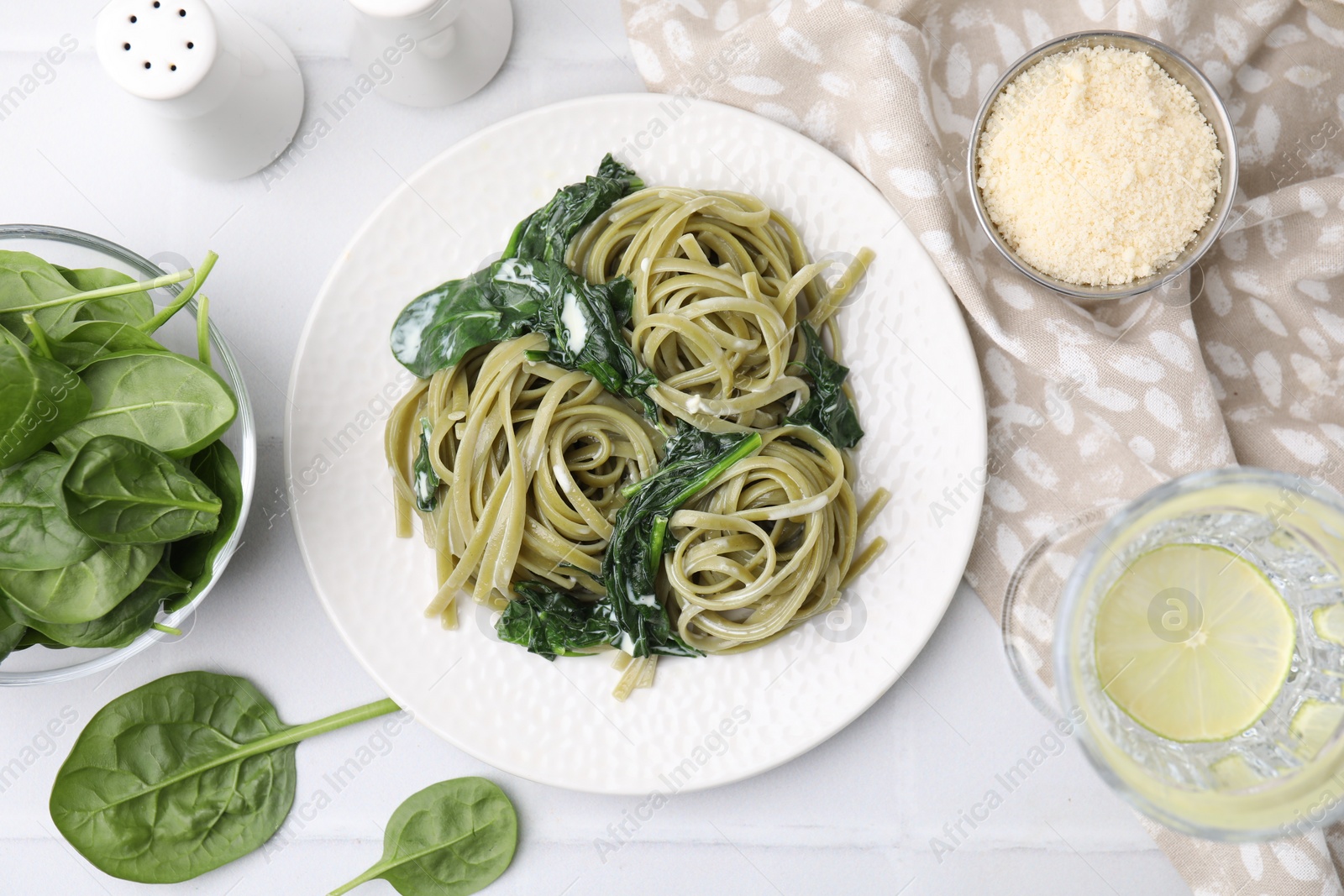 Photo of Tasty pasta with spinach and sauce served on white tiled table, flat lay