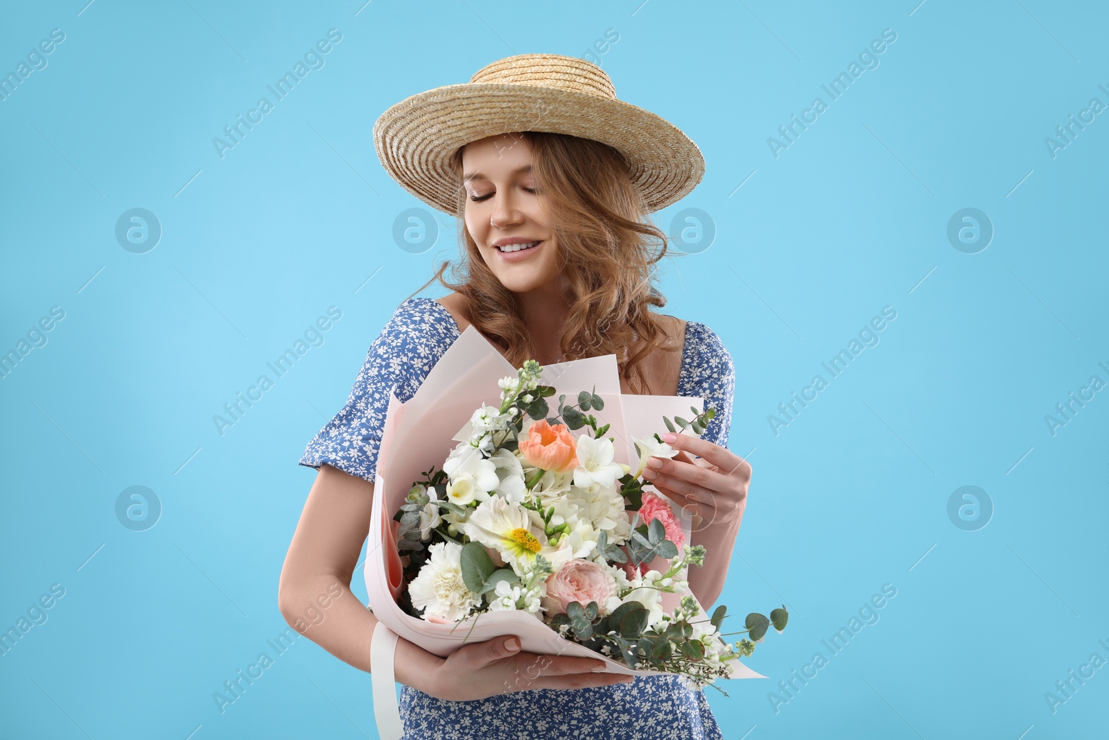 Photo of Beautiful woman in straw hat with bouquet of flowers on light blue background