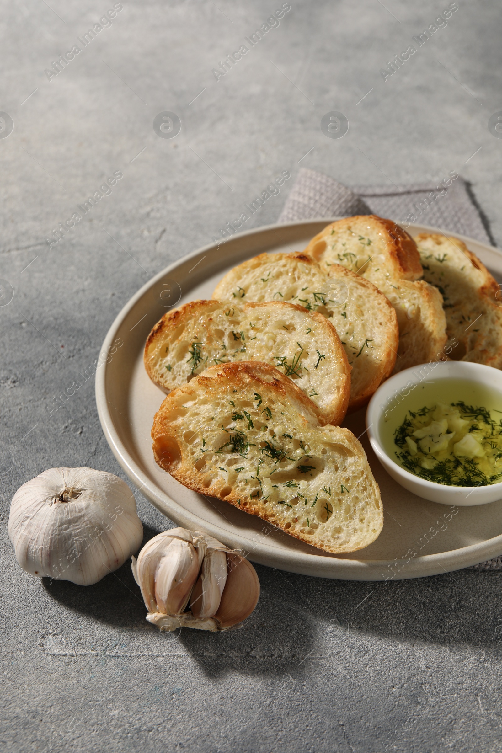 Photo of Tasty baguette with garlic and dill served on grey textured table