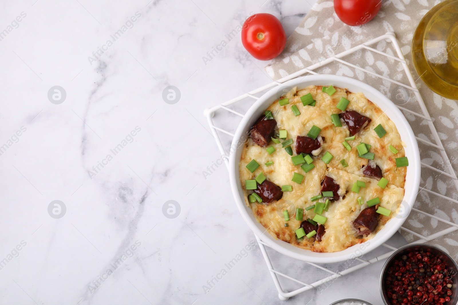 Photo of Tasty sausage casserole in baking dish and ingredients on white marble table, flat lay. Space for text