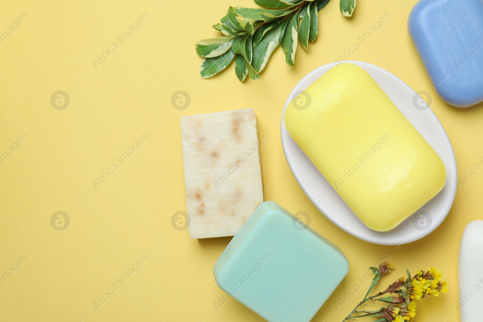 Photo of Many soap bars and plant branches on yellow background, flat lay. Space for text