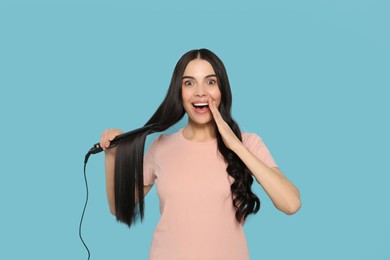 Beautiful emotional woman with hair iron on light blue background