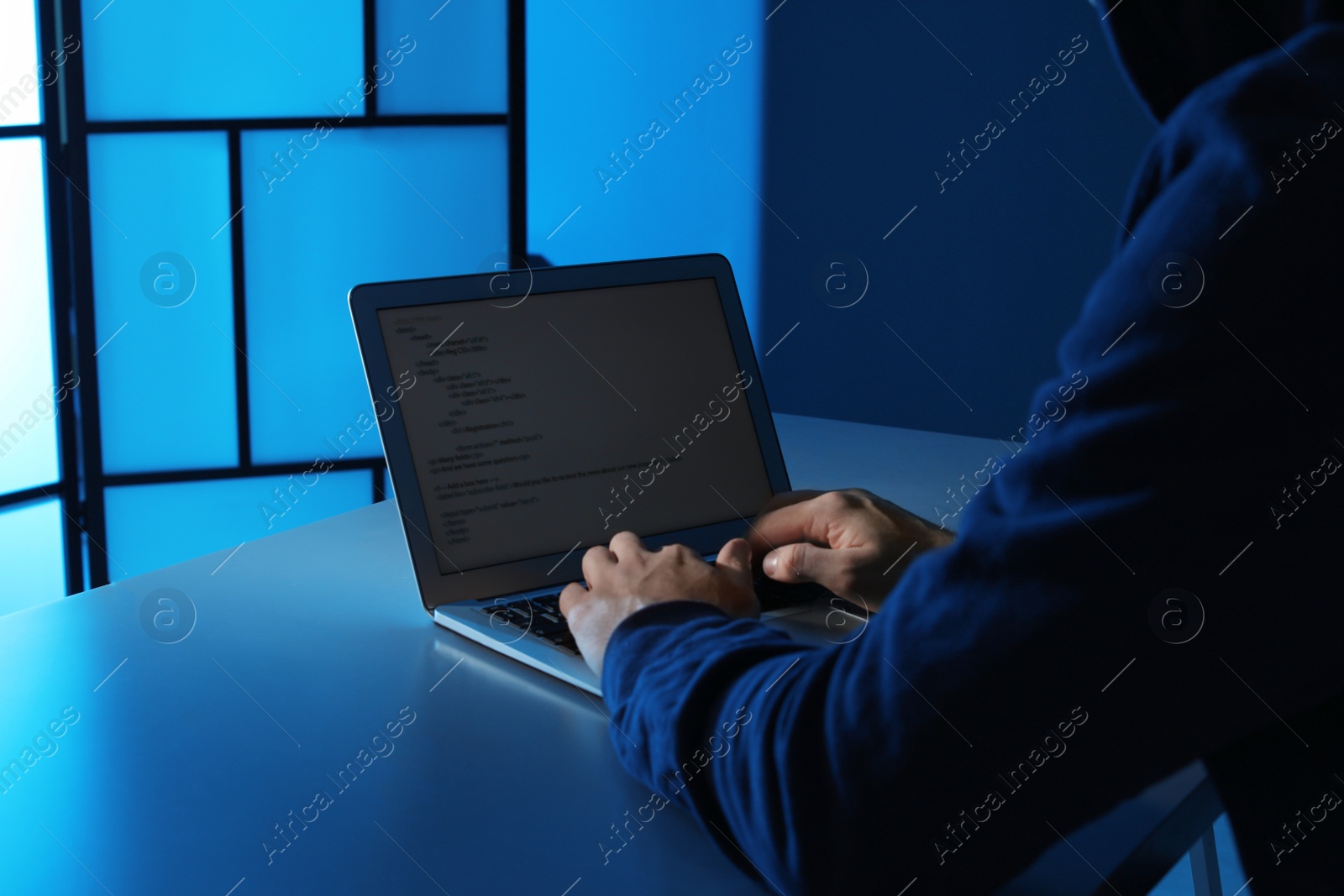 Photo of Man using laptop at table in dark room, closeup. Criminal offence