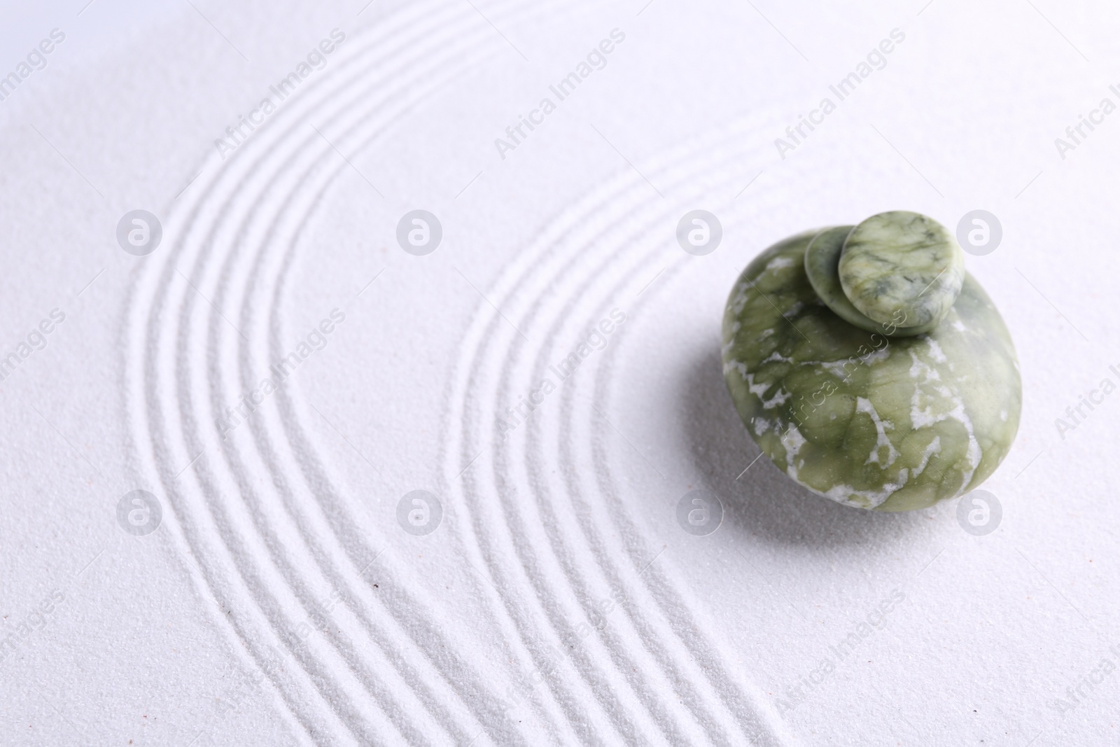 Photo of Zen garden stones on white sand with pattern. Space for text