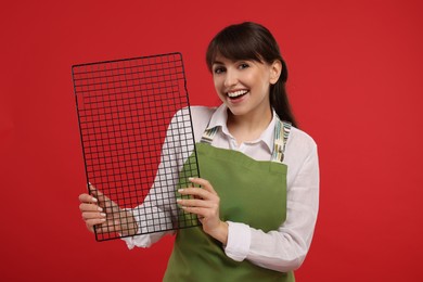 Photo of Happy professional confectioner in apron holding cooling rack on red background