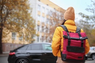 Photo of Female tourist with travel backpack on city street, back view. Urban trip