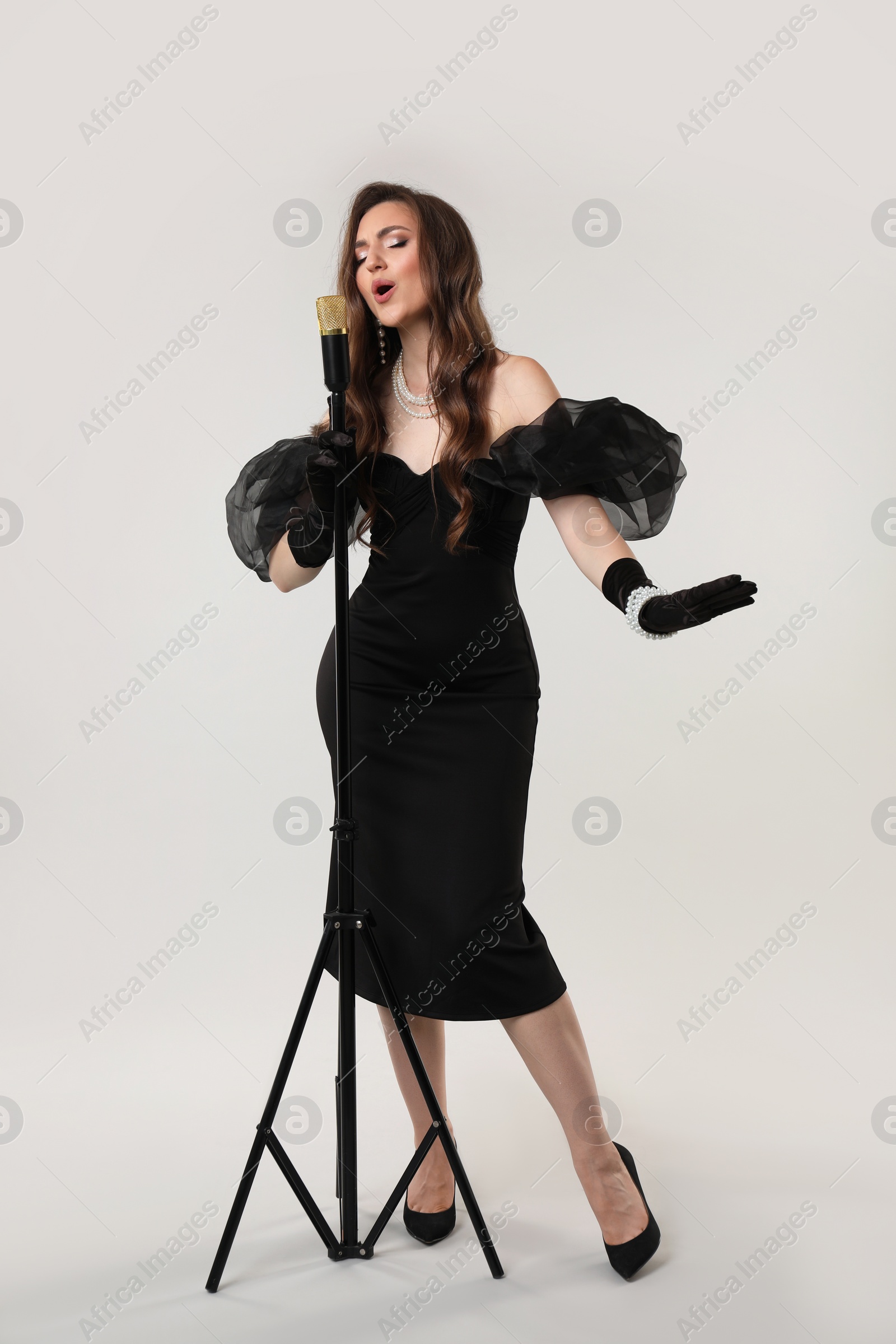 Photo of Beautiful young woman in stylish dress with microphone singing on light grey background