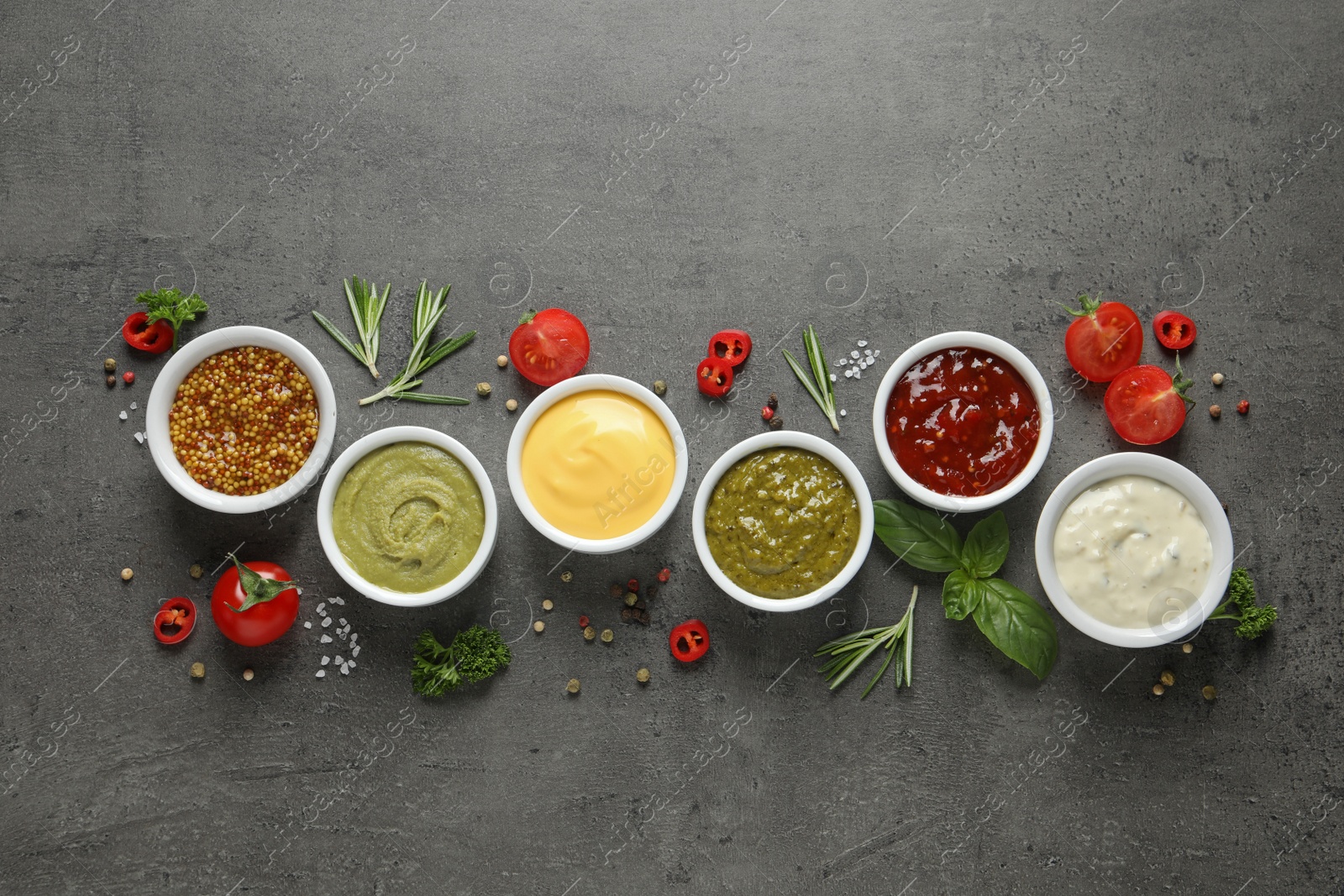 Photo of Bowls with different sauces and ingredients on gray background, flat lay