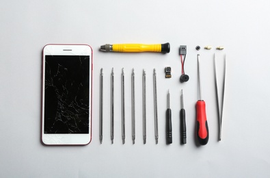 Photo of Composition with broken mobile phone and repair tools on white background, top view
