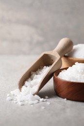 Photo of Natural salt in bowls and scoop on grey table, closeup