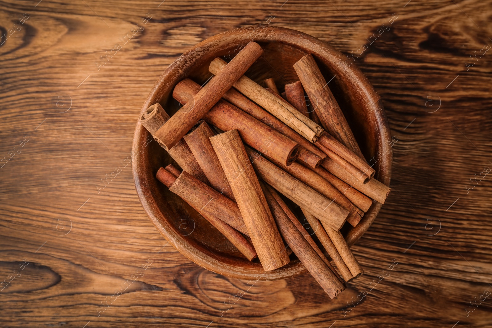 Photo of Bowl with aromatic cinnamon sticks on wooden background