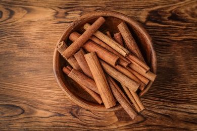 Bowl with aromatic cinnamon sticks on wooden background