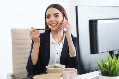 Office employee having salad for lunch while talking on phone at workplace. Food delivery