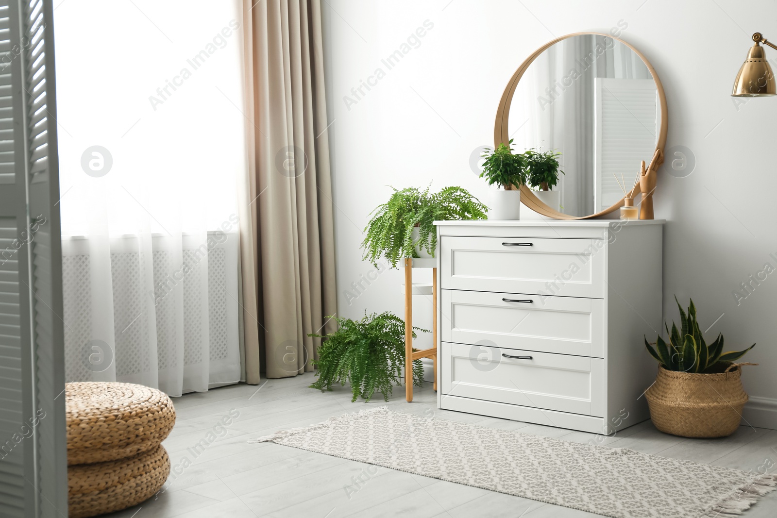 Photo of Round mirror and chest of drawers near white wall in room. Modern interior design