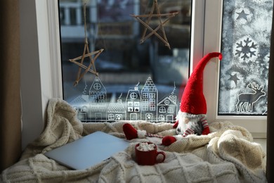 Photo of Gnome, laptop and hot drink on knitted plaid near window with beautiful drawing at home. Christmas decor