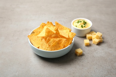 Photo of Bowl of delicious mexican nachos chips and cheese sauce on grey table