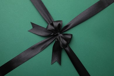 Photo of Black satin ribbon with bow on green background, top view