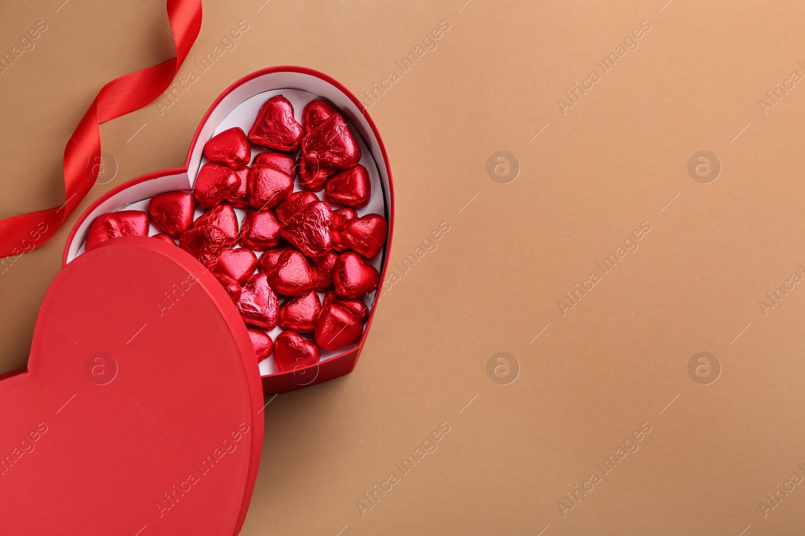 Photo of Box of heart shaped chocolate candies and ribbon on brown background, flat lay. Space for text