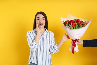 Happy woman receiving red tulip bouquet from man on yellow background. 8th of March celebration