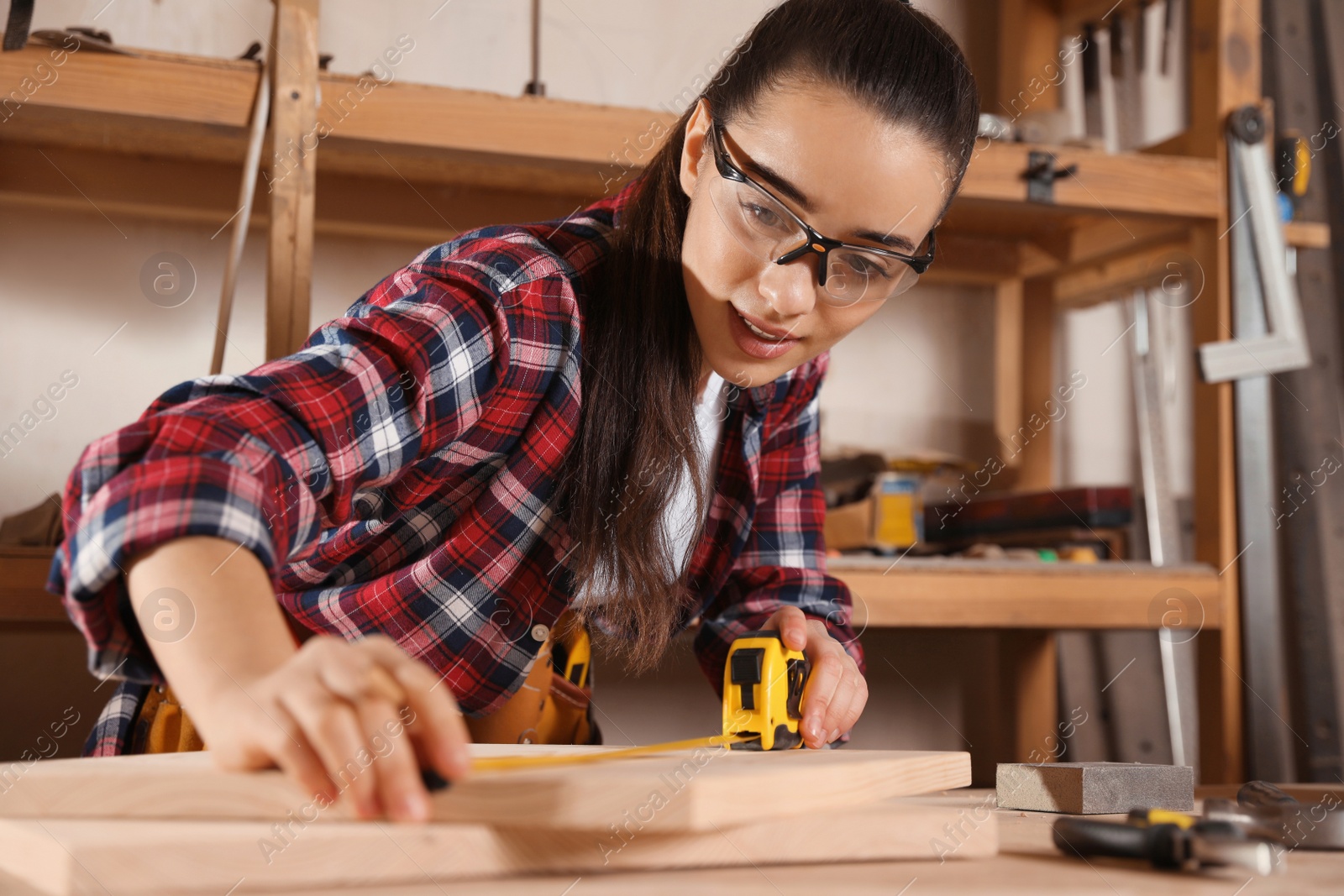 Photo of Female carpenter measuring wooden board in workshop