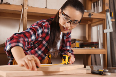 Female carpenter measuring wooden board in workshop