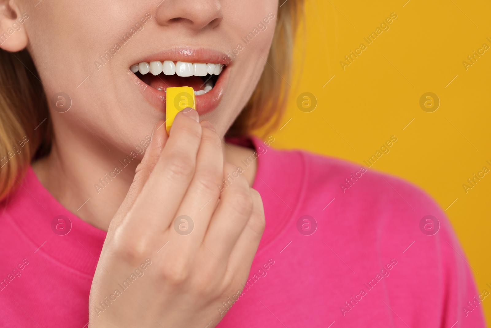 Photo of Woman putting bubble gum into mouth on yellow background, closeup