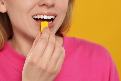 Woman putting bubble gum into mouth on yellow background, closeup