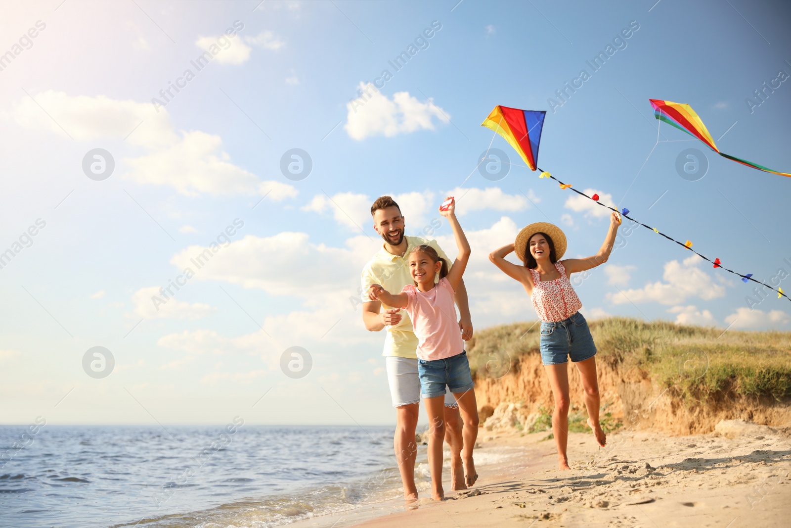 Photo of Happy parents and their child playing with kites on beach near sea. Spending time in nature