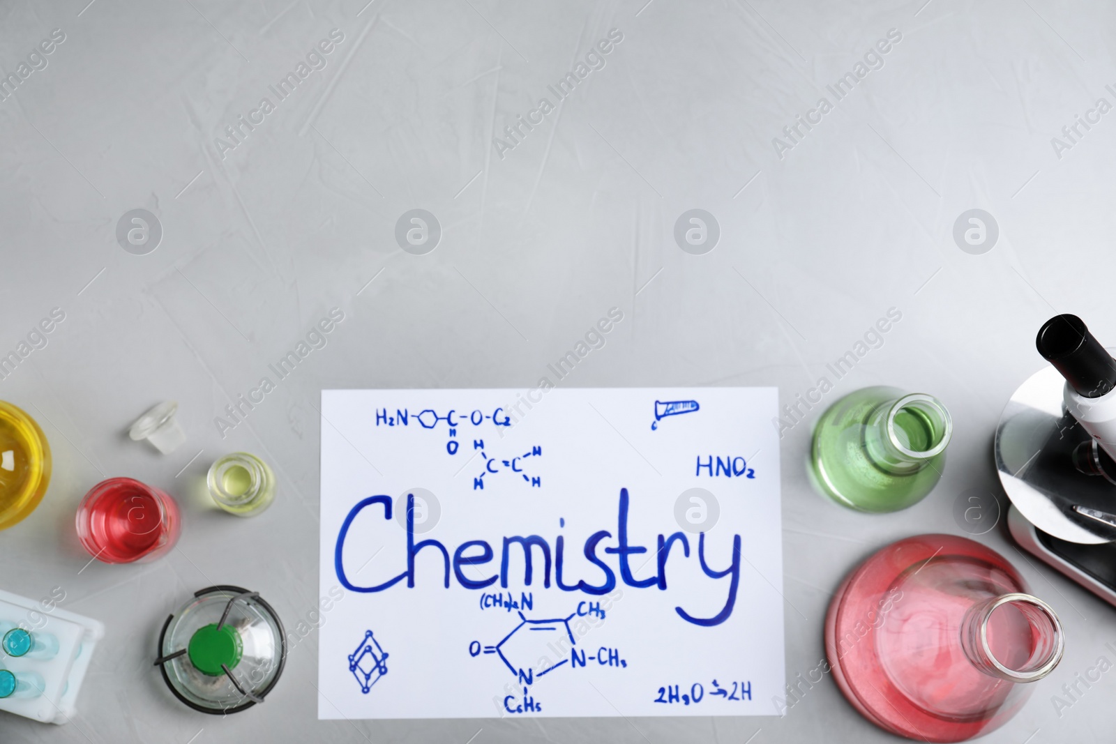 Photo of Laboratory glassware and paper with word CHEMISTRY on grey background, top view. Space for text