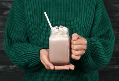 Photo of Woman holding mason jar of delicious cocoa drink with marshmallows, closeup