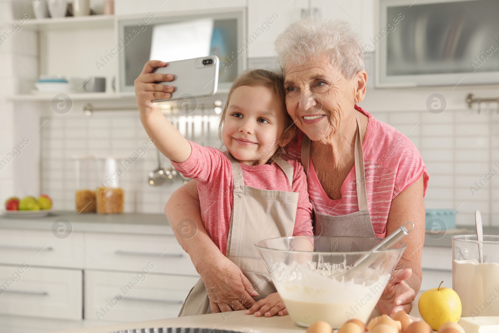 Photo of Little girl and her grandmother taking selfie in kitchen