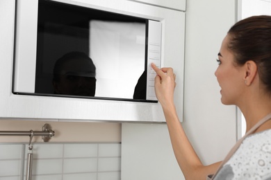 Photo of Young woman using microwave oven at home