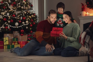 Happy family opening gift box with magical light at home. Christmas celebration