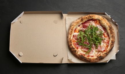 Tasty pizza with meat and arugula in cardboard box on black table, top view