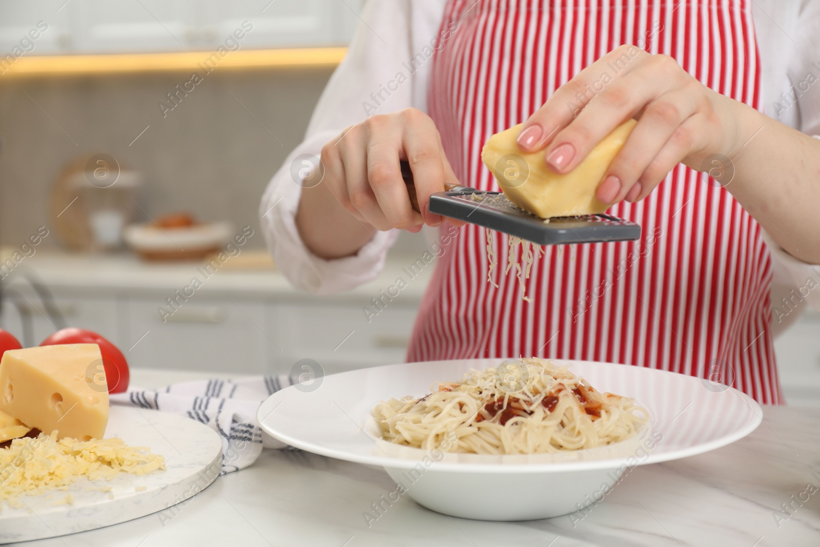 Photo of Woman grating cheese onto delicious pasta at white marble table in kitchen, closeup