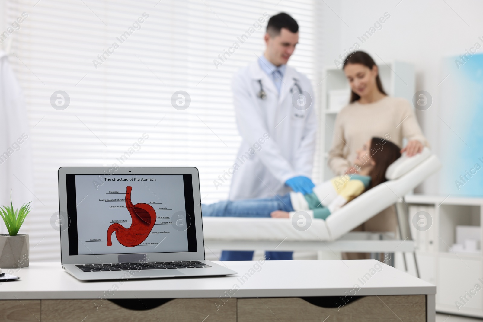 Photo of Gastroenterologist examining girl in clinic, focus on laptop with image of stomach on white table