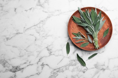 Photo of Wooden plate with fresh green sage on white marble  table, flat lay. Space for text
