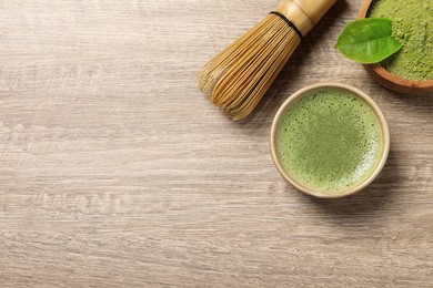 Photo of Cup of fresh matcha tea, bamboo whisk and green powder on wooden table, flat lay. Space for text