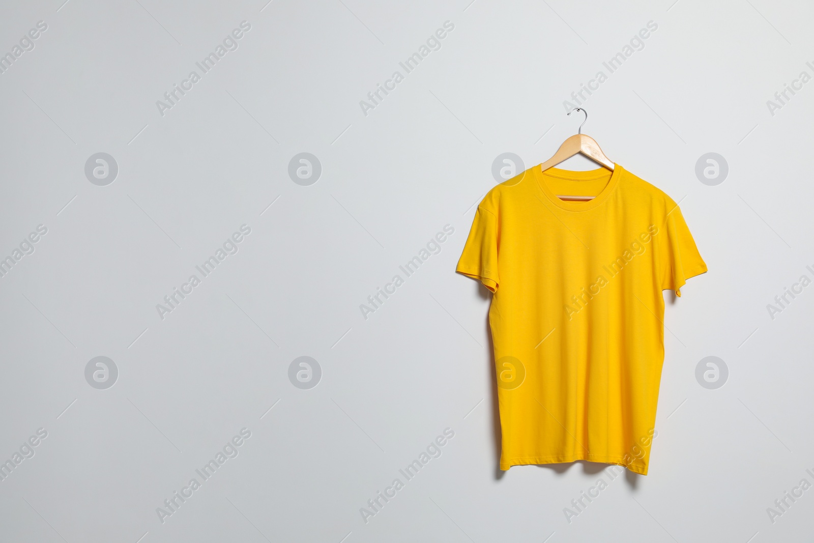 Photo of Hanger with yellow t-shirt on light wall. Mockup for design