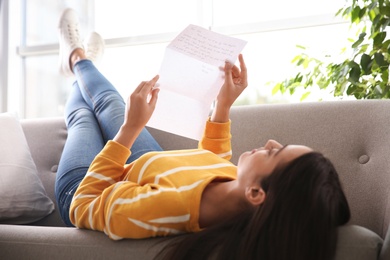 Photo of Woman reading letter on sofa at home, focus on hands