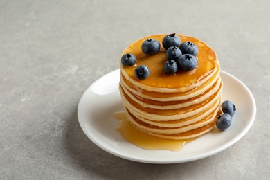 Plate with pancakes and berries on grey background