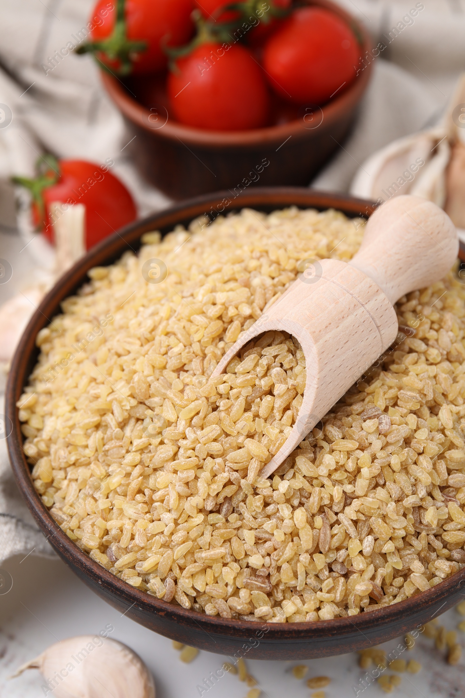 Photo of Bowl and scoop with raw bulgur on table, closeup