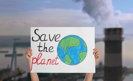 Image of Protestor holding placard with text Save The Planet and blurred view of industrial factory on background. Climate strike