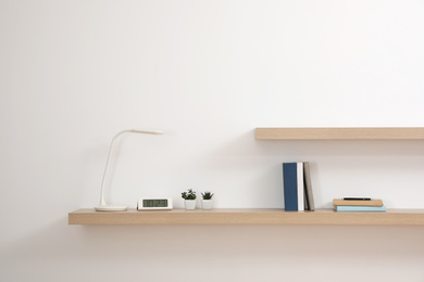 Photo of Wooden shelves with books and decorative elements on light wall