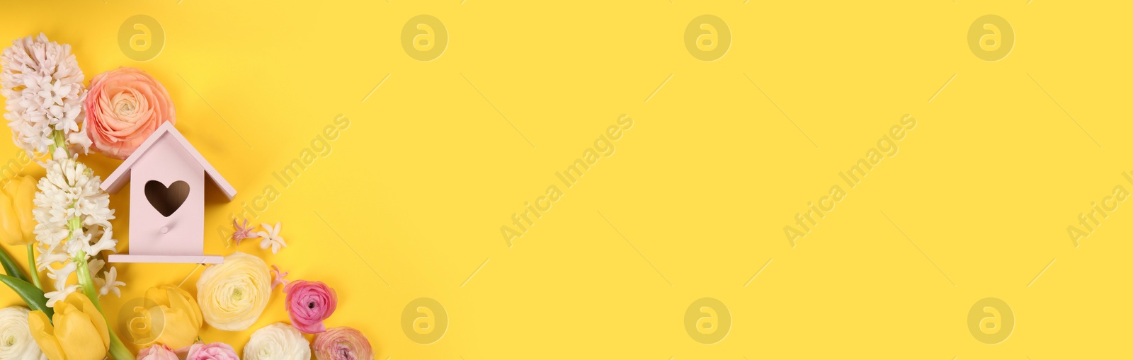 Photo of Stylish bird house and fresh flowers on yellow background, flat lay. Space for text