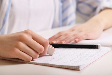 Photo of Girl erasing mistake in her notebook at white desk, closeup