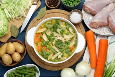 Photo of Saucepan of delicious vegetable soup with chicken and different ingredients on blue wooden table, flat lay