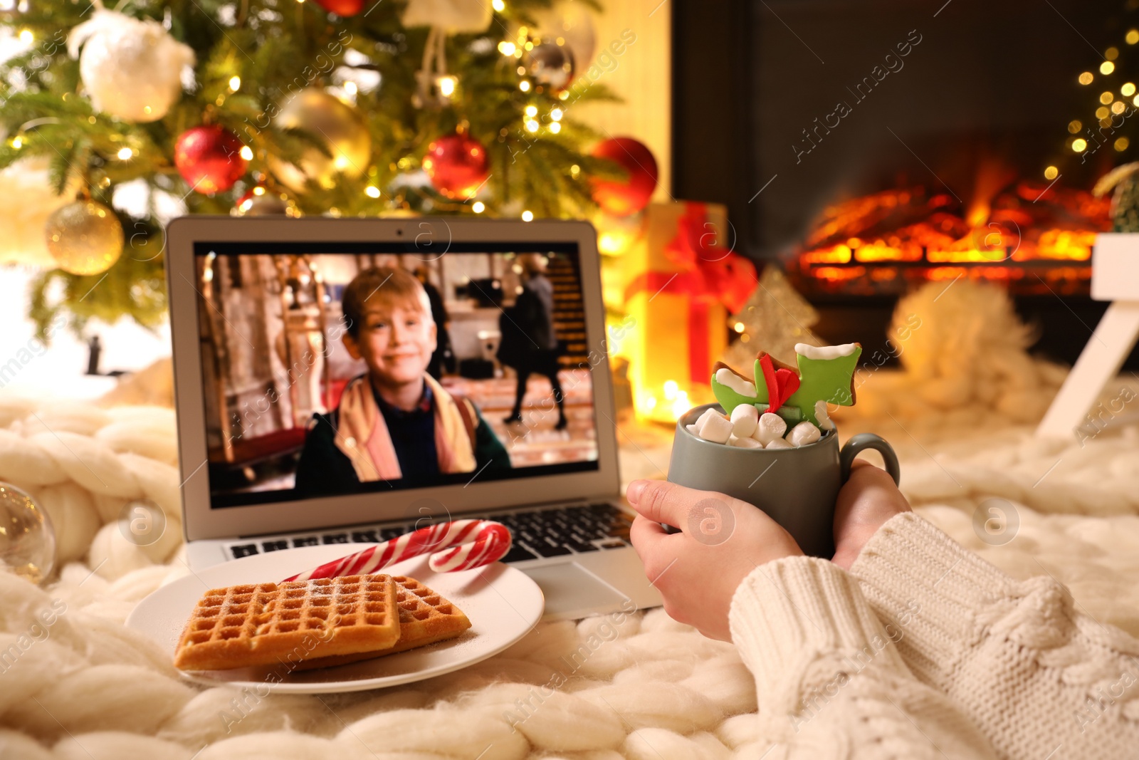 Photo of MYKOLAIV, UKRAINE - DECEMBER 23, 2020: Woman with sweet drink watching Home Alone movie on laptop at home, closeup. Cozy winter holidays atmosphere