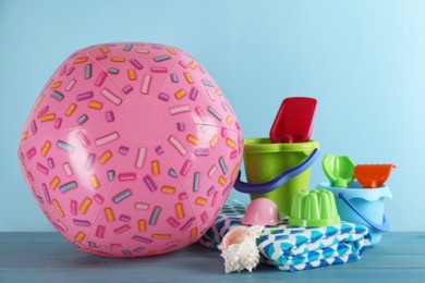 Pink beach ball, blanket, shell and sand toys on light blue wooden table